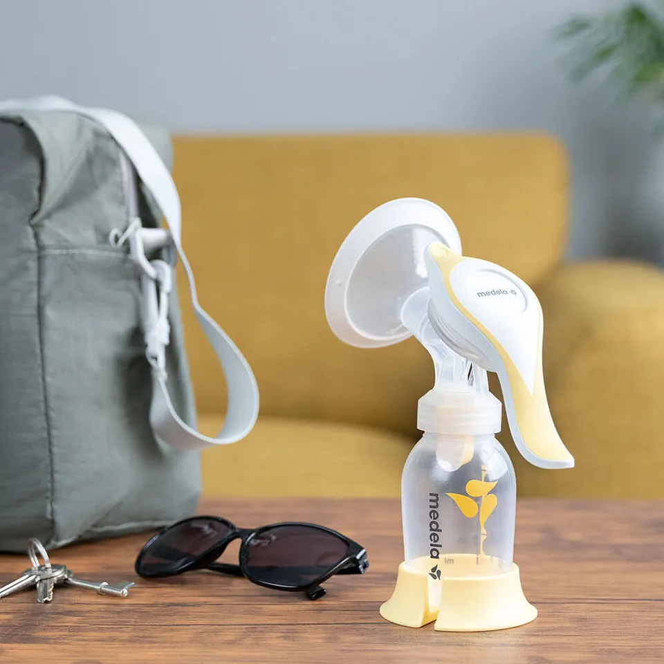 Medela Harmony manual pump on a table beside sunglasses and a bag.