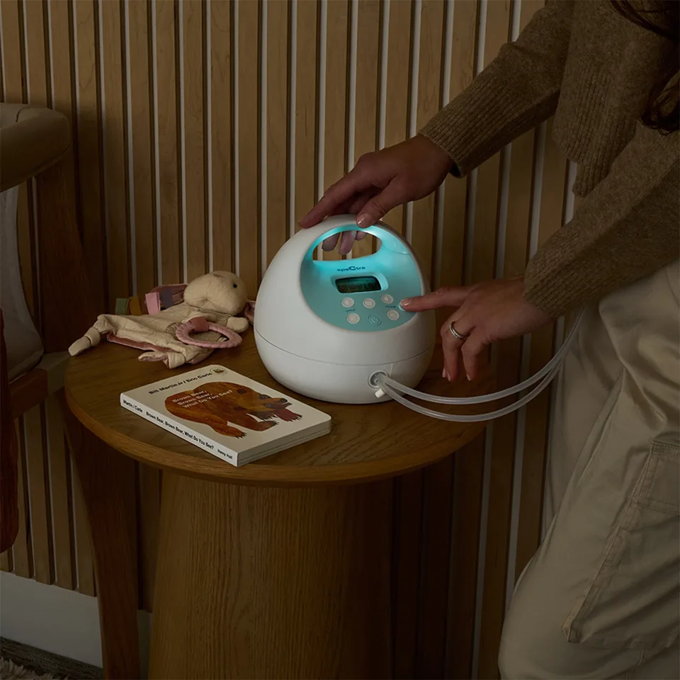 Hand adjusting the controls of a Spectra S1 Plus on a round bedside table.