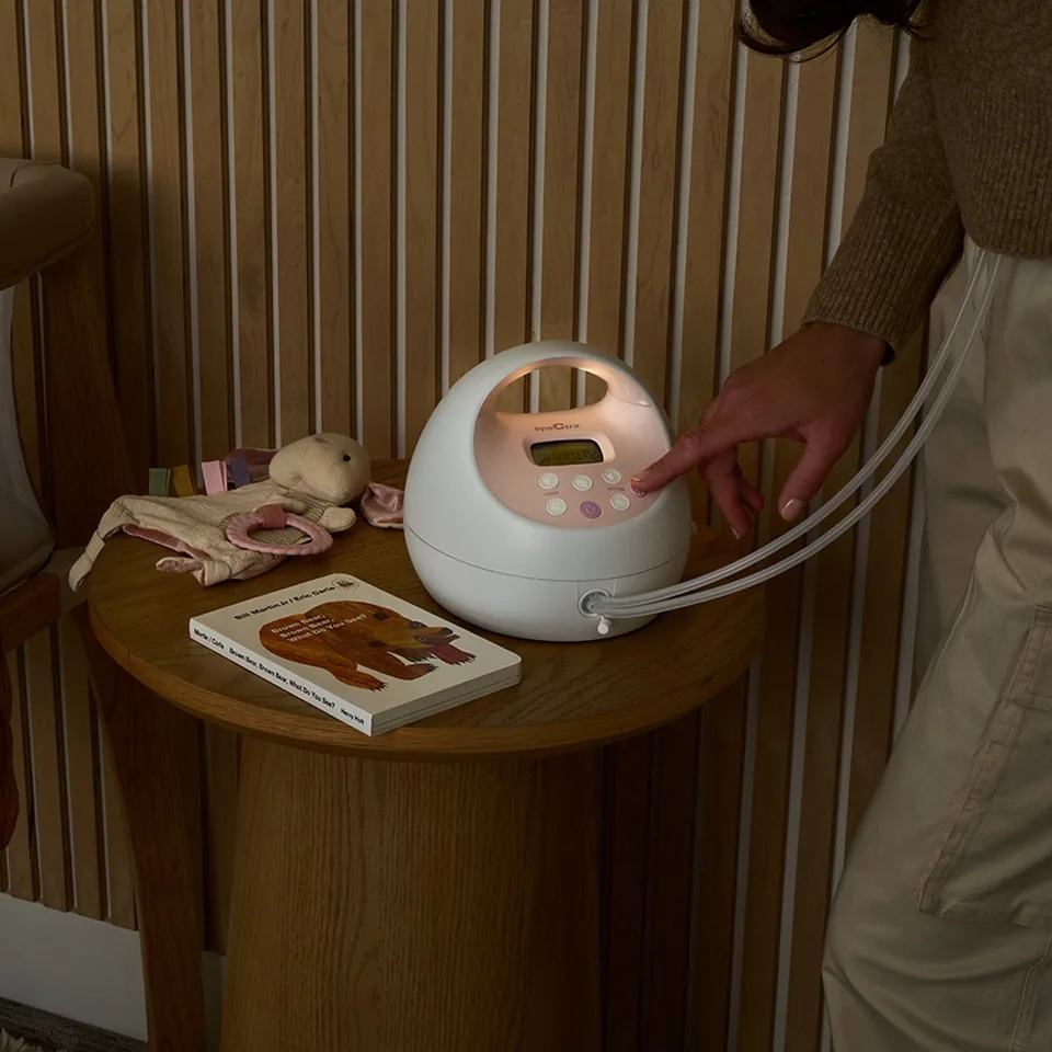 Hand pressing the controls of a Spectra S2 Plus on a round bedside table.