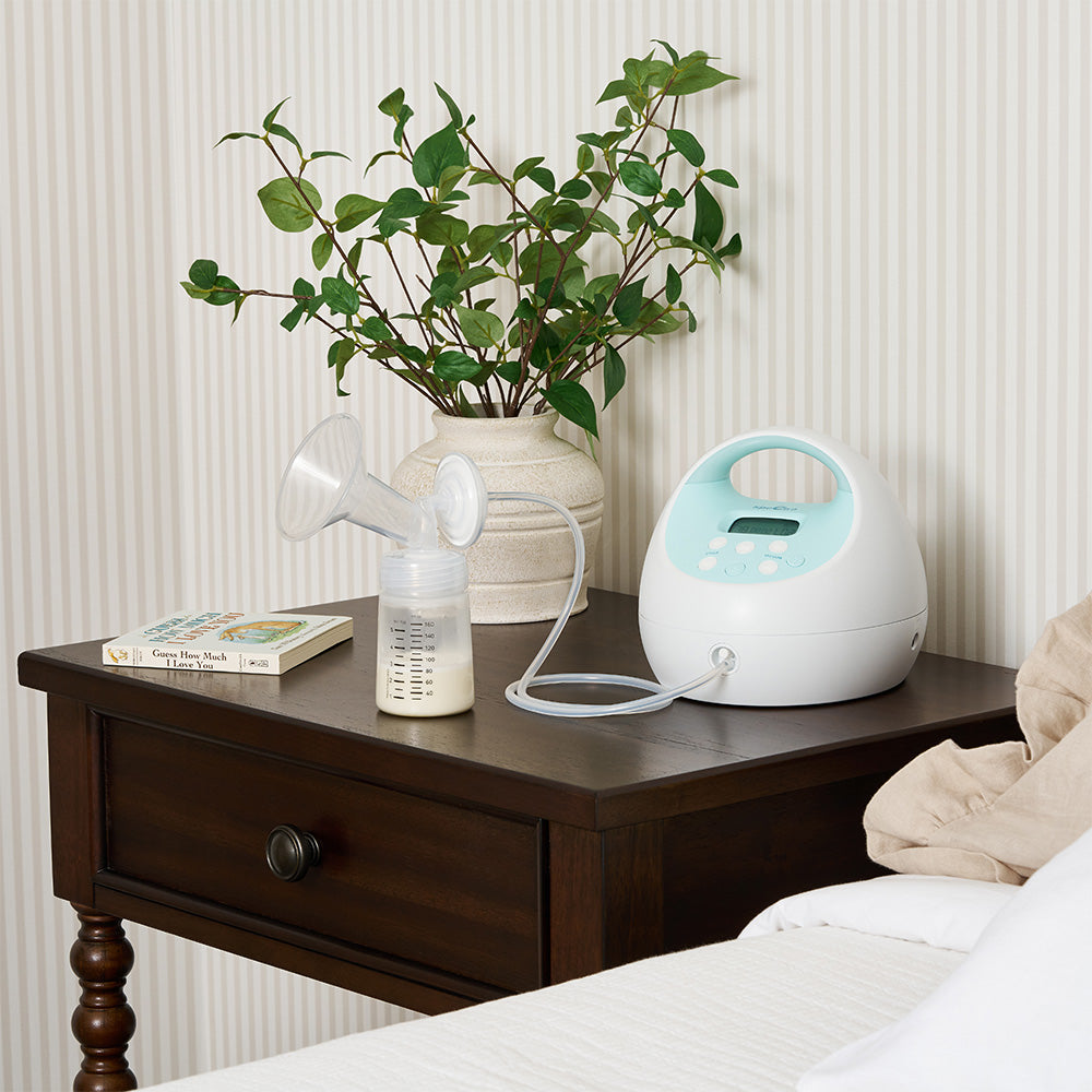 A Spectra S1 Plus breast pump and collection bottle on a bedside table